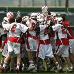group of lacrosse players celebrating with coach during daytime
